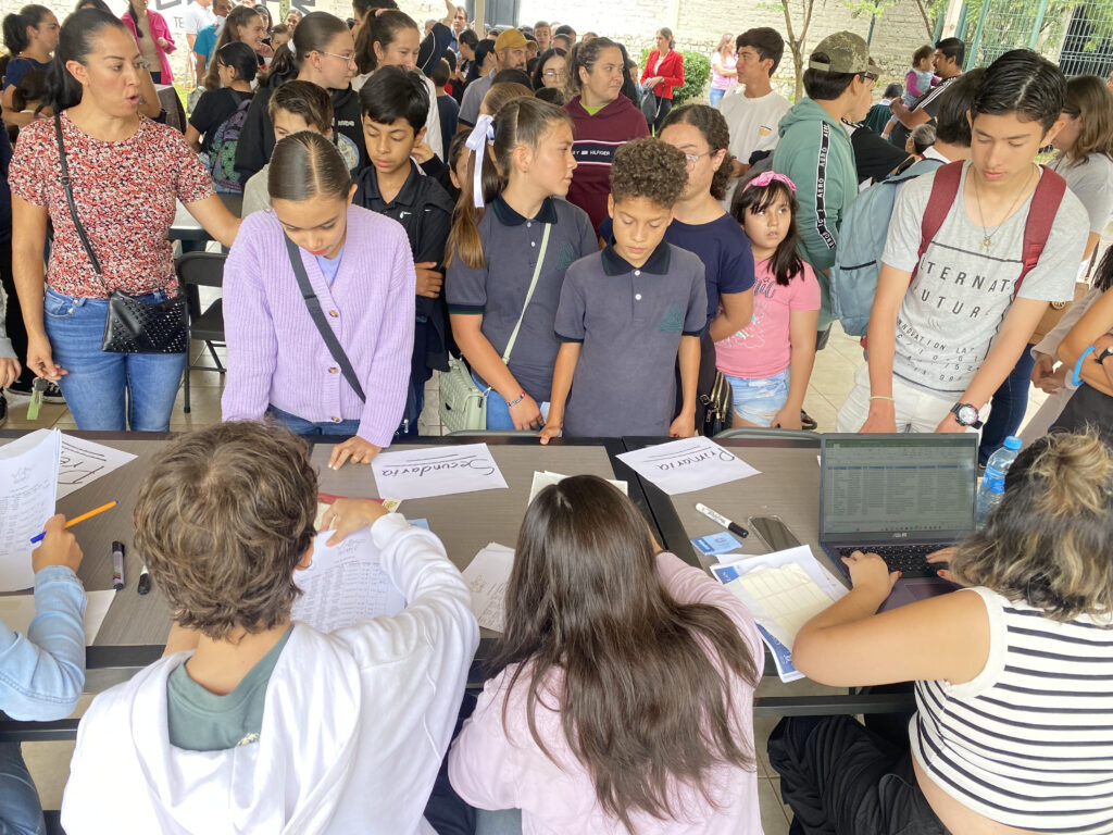 Familias y estudiantes haciendo fila en las mesas de registro de la OMPiT 2025